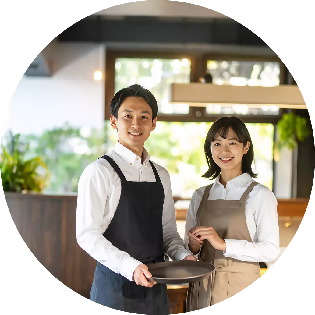 飲食店で、白シャツにエプロン姿の男性と女性が並んで立っている画像