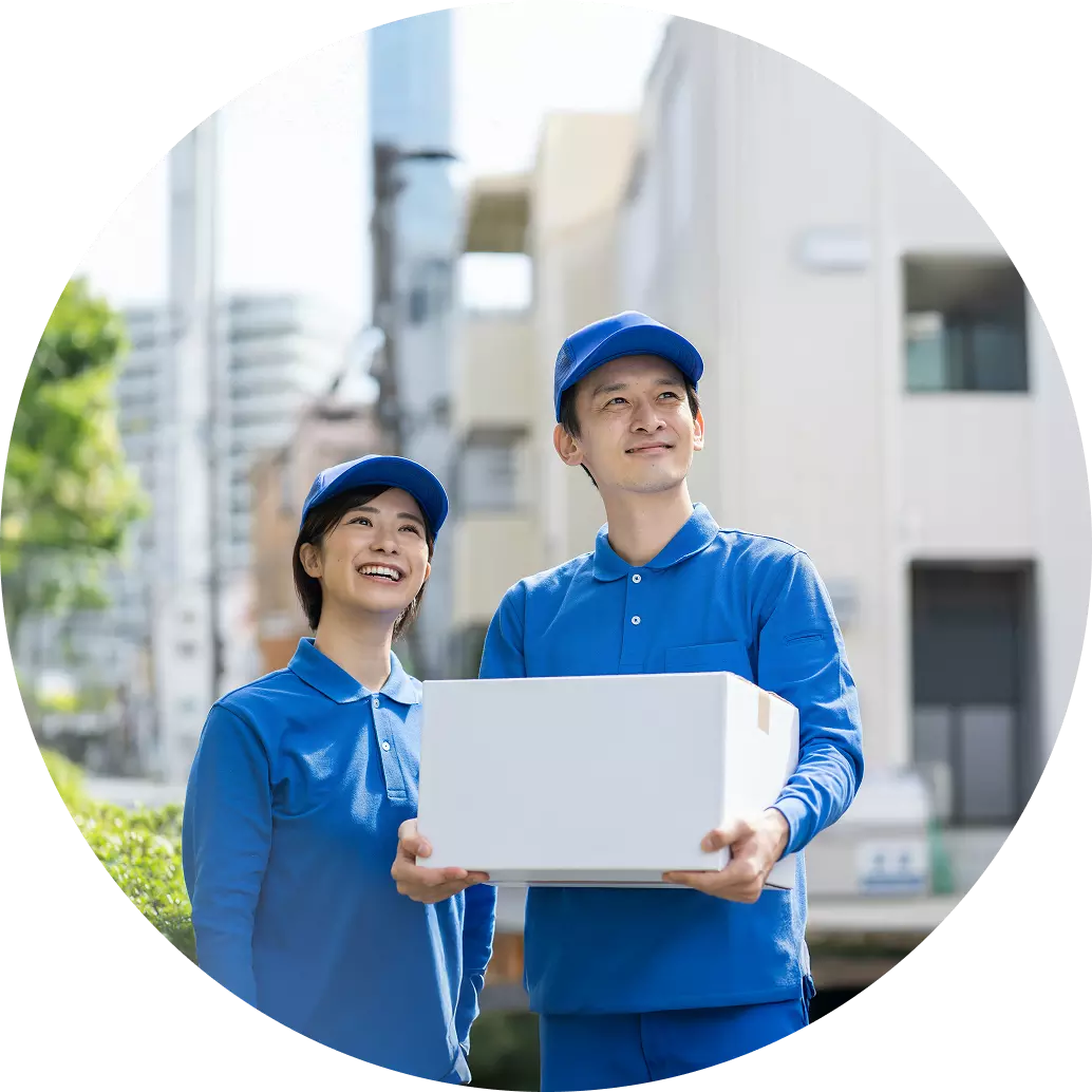 住宅街で、青い制服と帽子を着用した男性と女性の配達員が白い箱を持って並んで立っている画像